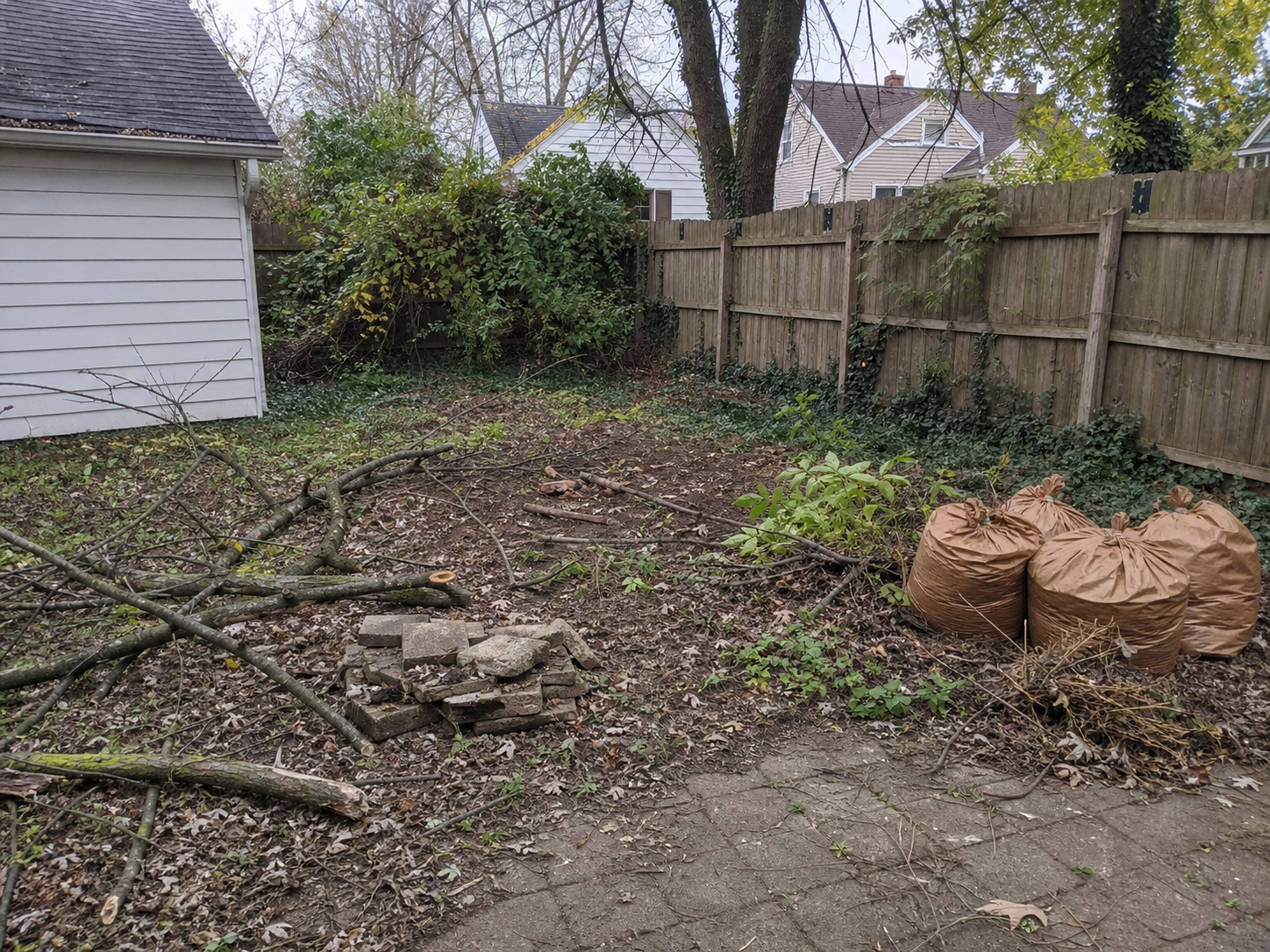 Backyard with branches, bagged leaves, and yard debris before cleanup
